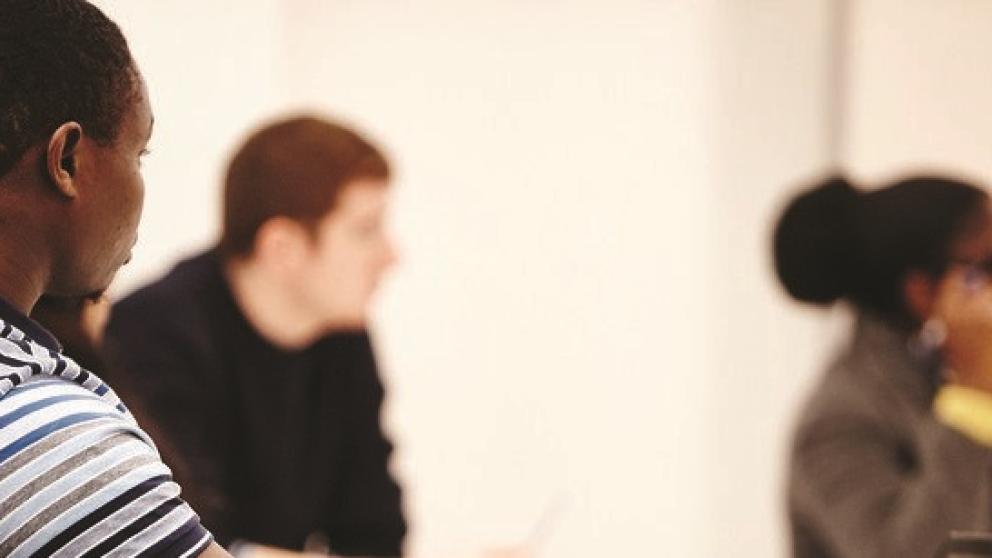 Three students sit in a classroom looking at something out of frame. 