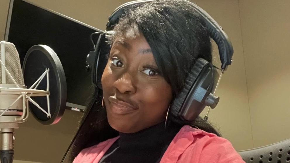 Actress Grace McIntosh stood at a microphone with headphones on. 