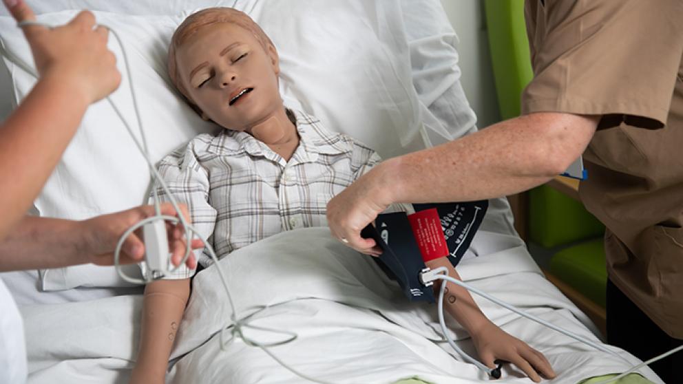 A medical mannequin of a child in a hospital bed being used by medical students. 