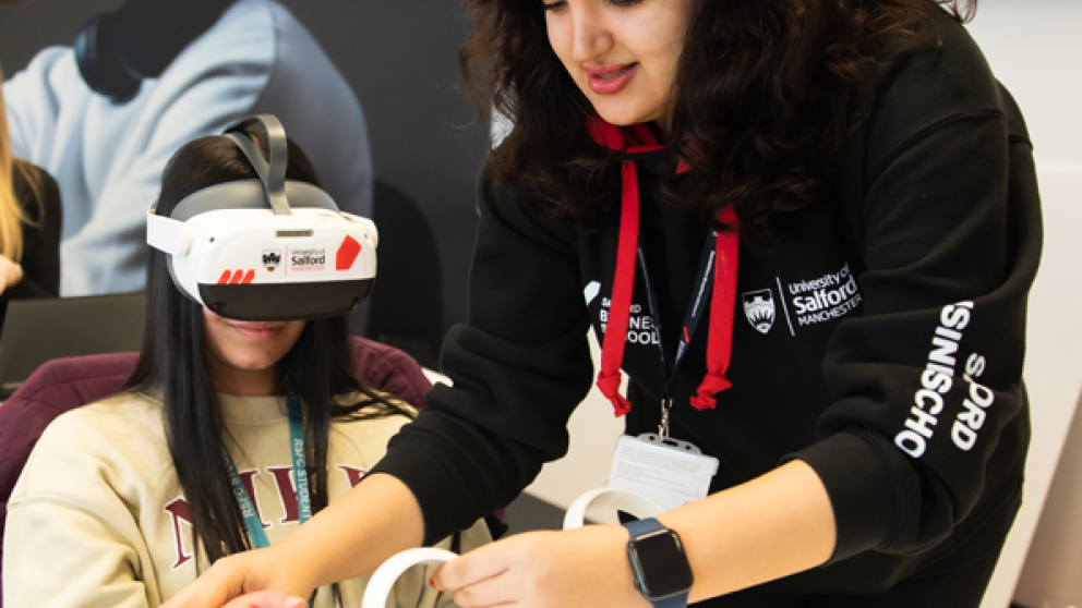 Student wearing a VR headset in a classroom getting assistance from another woman. 
