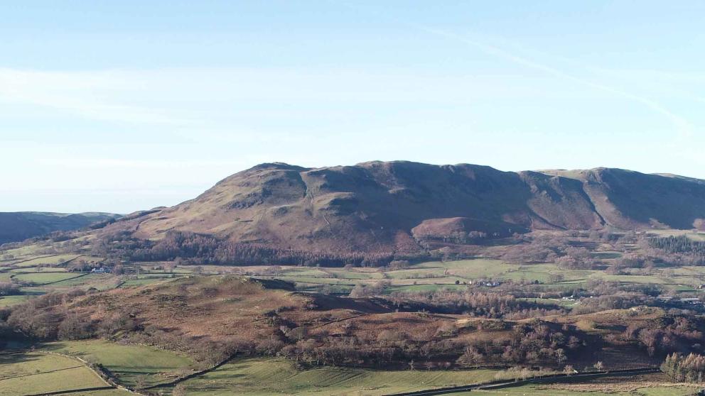 Dried up riverbed cutting through fields, with hills in the background
