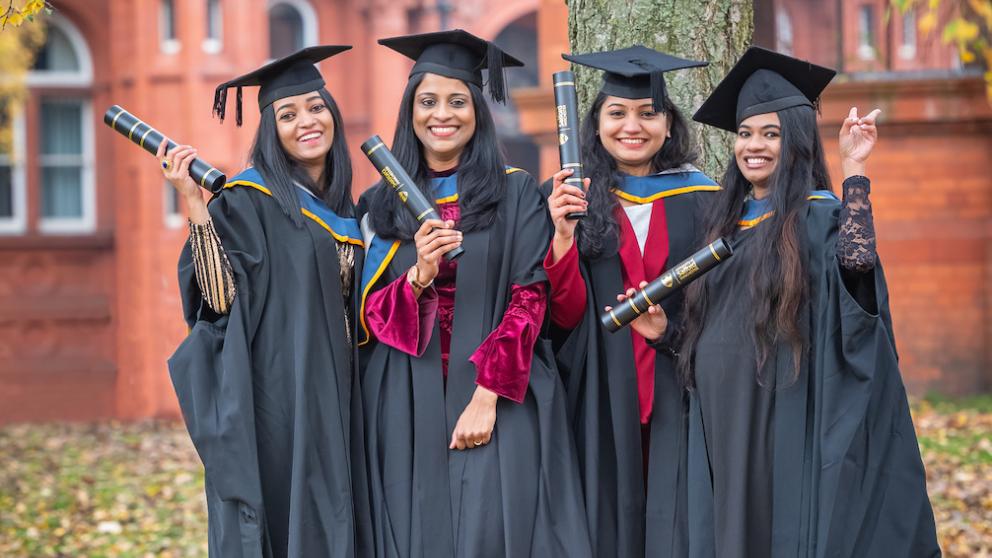 Graduates posing in front of a tree outside the Peel Building