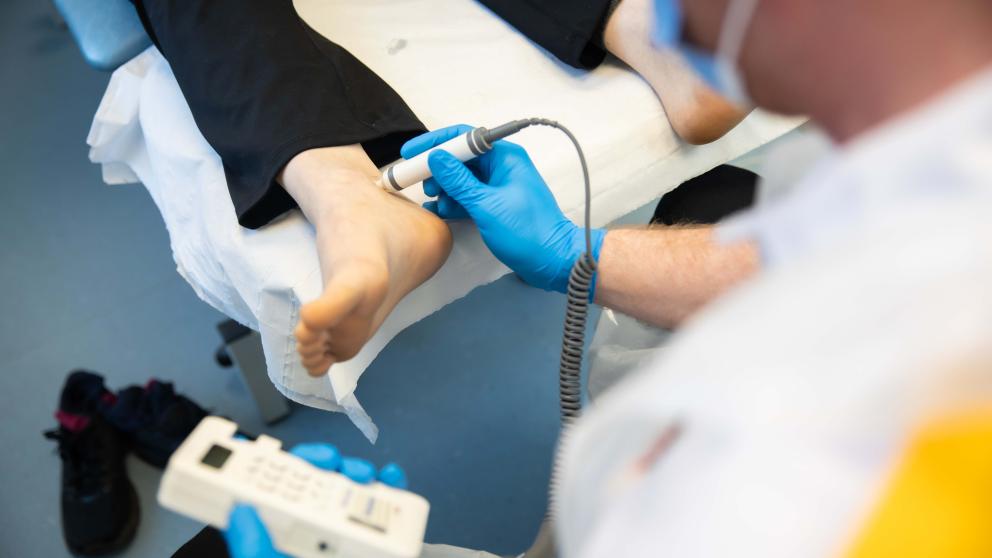 A podiatry apprentice using a tool on a patients foot 