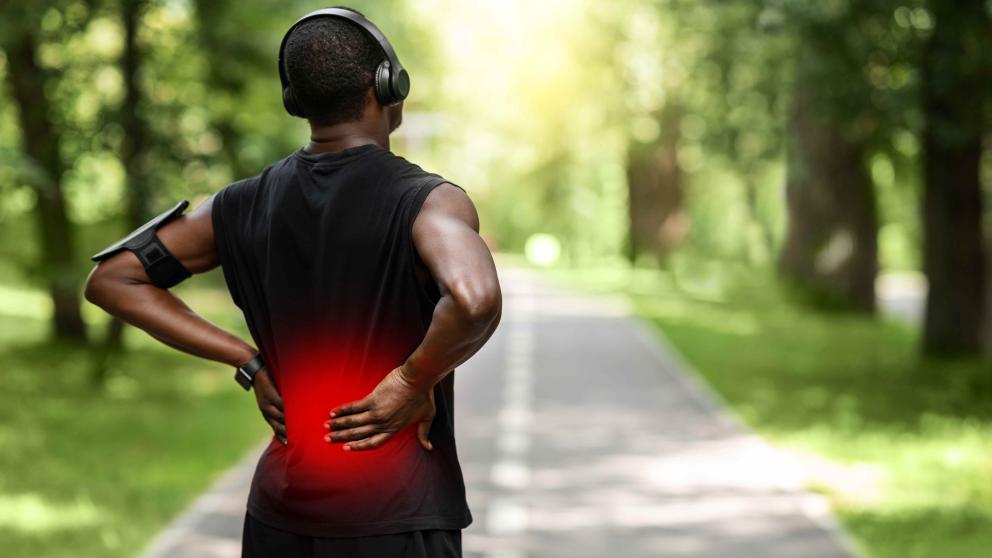 Image shows a male runner holding his back