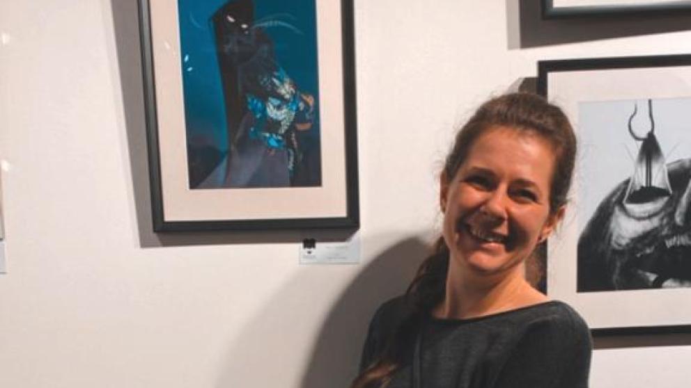 A female student stood next to her illustration framed on a wall