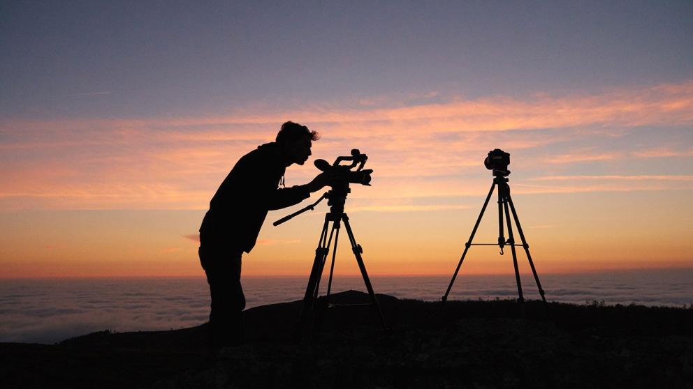 Silhouette of person with two cameras on tripods in the sunset