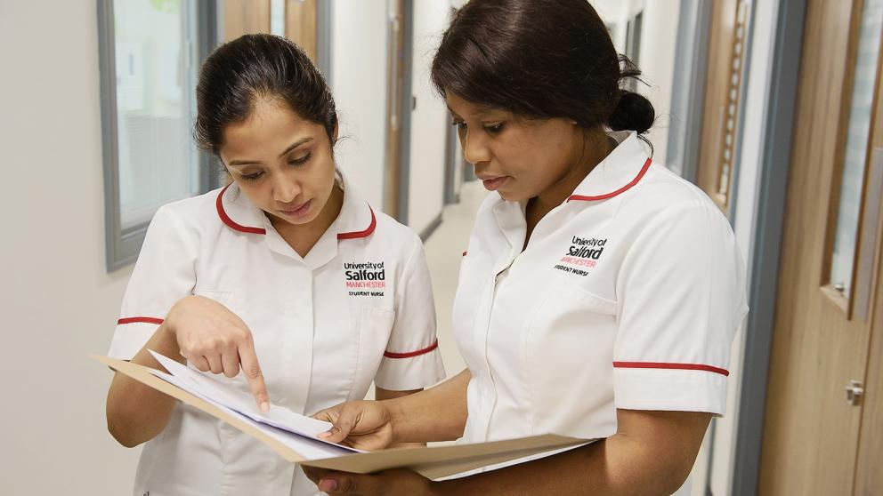 Two nursing students looking over nursing records in paper folder together