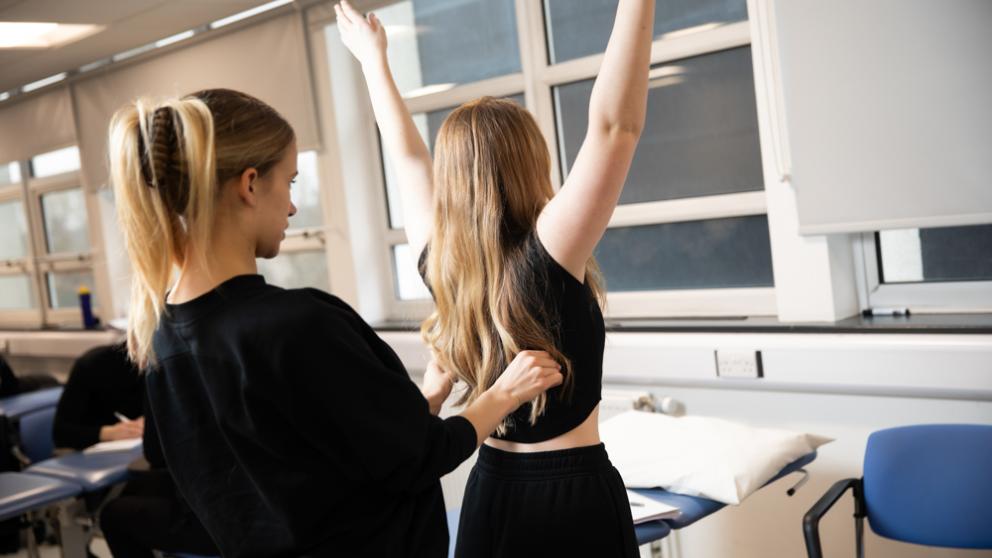 Female student standing behind another conducting a musculoskeletal assessments