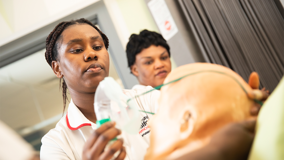 Female nursing student placing a nebulizer mask on a 'patient' manakin.