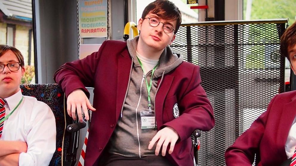 Three boys sit in school uniform on a mobility bus