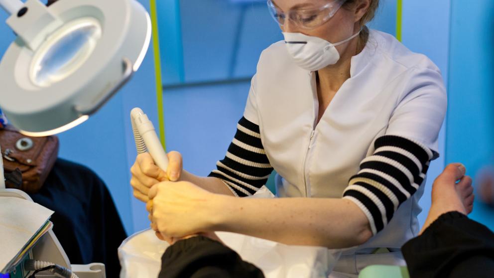Podiatry degree student using equipment on a patient's foot.