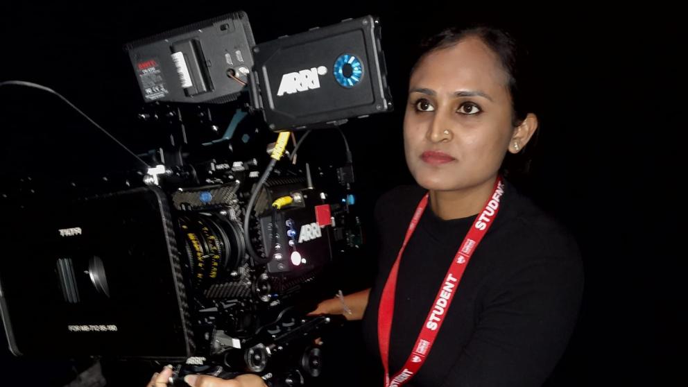 A female student holding a camera looking towards what she is filming