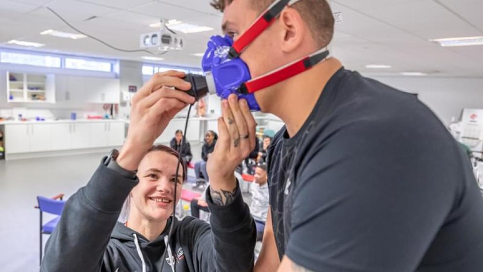 A female student fitting a CO₂ analysis device on a male participant in a laboratory setting