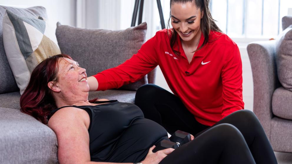Dr Ashley Gluchowski supporting a lady to do strength training in her living room