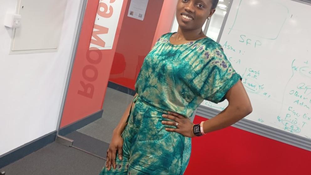 A female student wearing a patterned green jumpsuit smiling at the camera with a hand on her hip