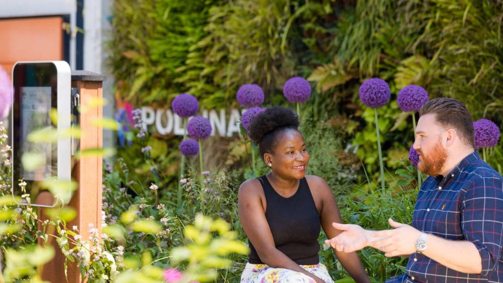 Two colleagues in the Ignition Garden, positioned in front of the Green Wall outside the Cockcroft Building at the University of Salford