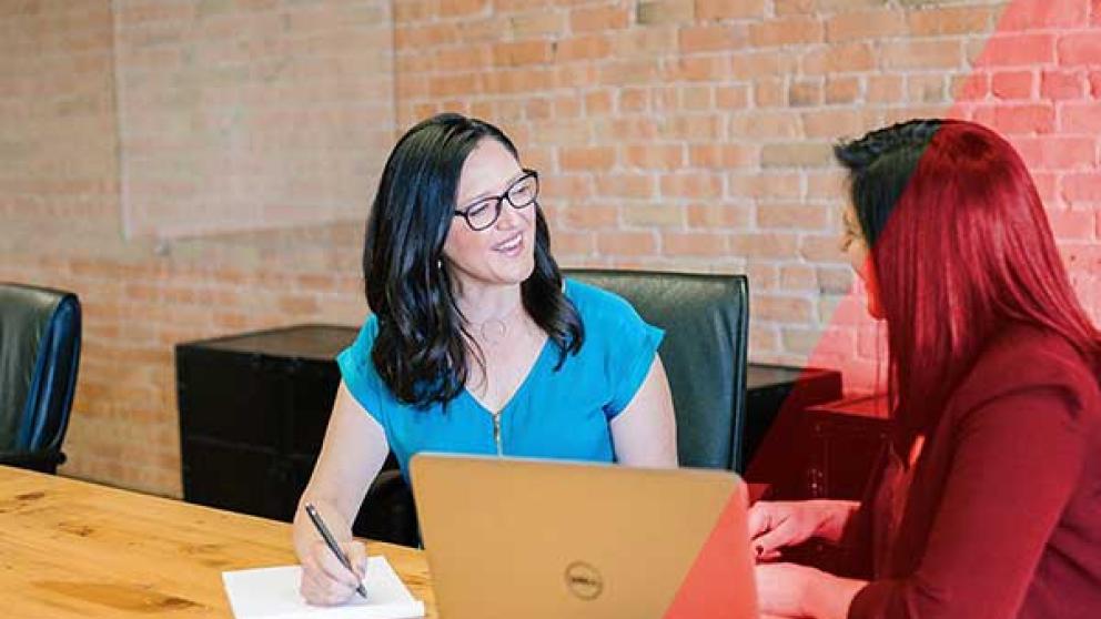 Two people seated at a table have a discussion 