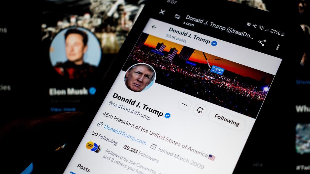 A smartphone screen displays Donald Trump's X account with Elon Musk in the background