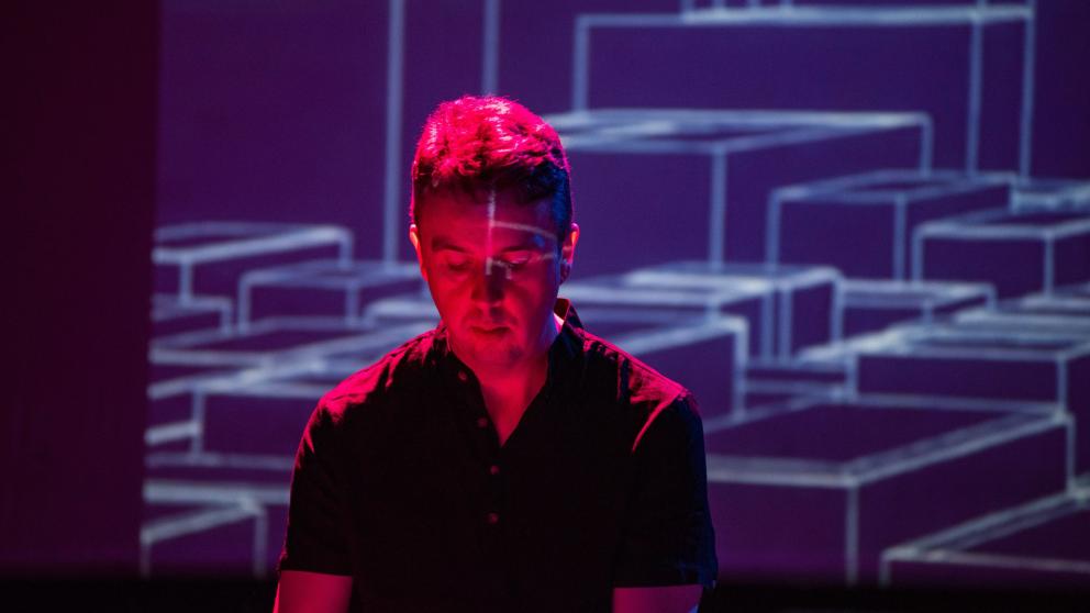 A man is photographed with a red hue and technological scene behind him