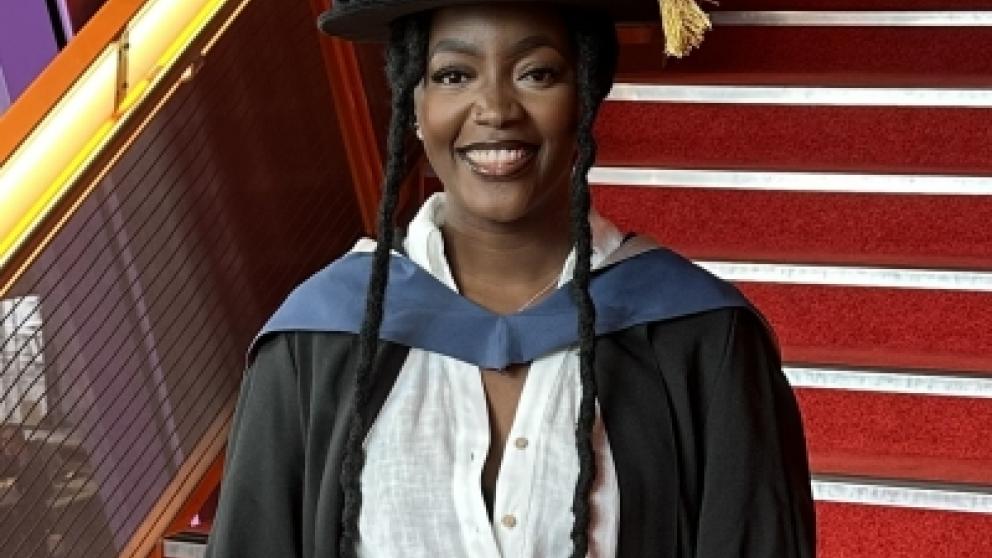 Peninah smiles at camera wearing her academic robes