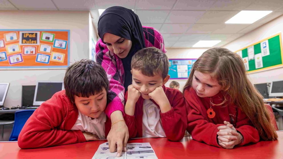 Female helper in headscarf helping pupils in school 