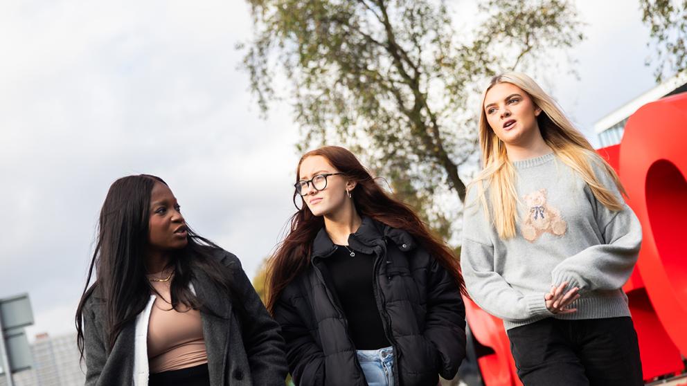 Three Students walking past the Salford Sign.