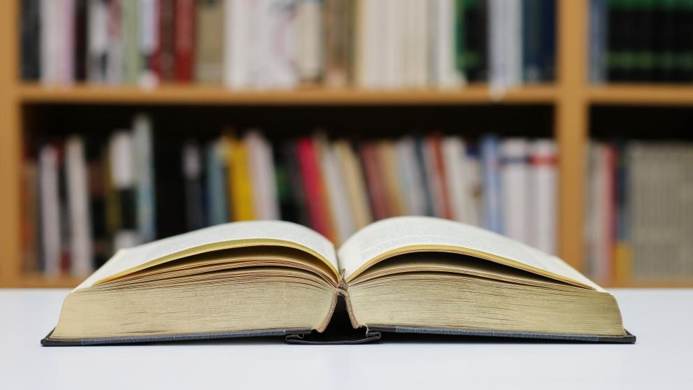 An open book stands on a table within a library