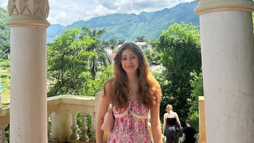 A student stood between two ornate columns in front of mountains in Vietnam