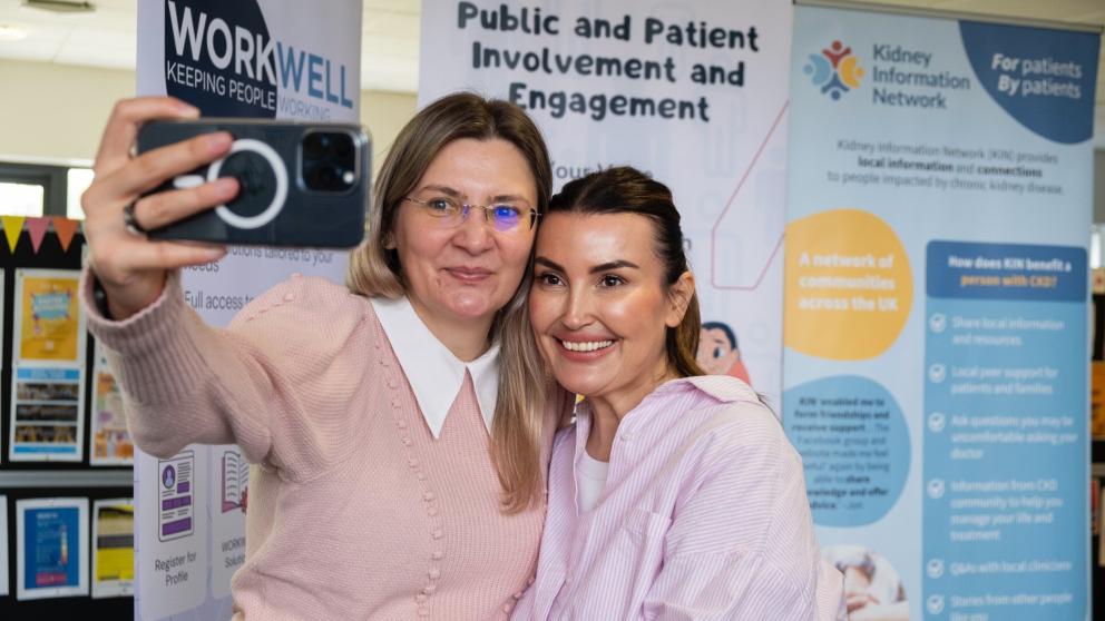 Two researchers smile as they take a selfie in front of roller banners