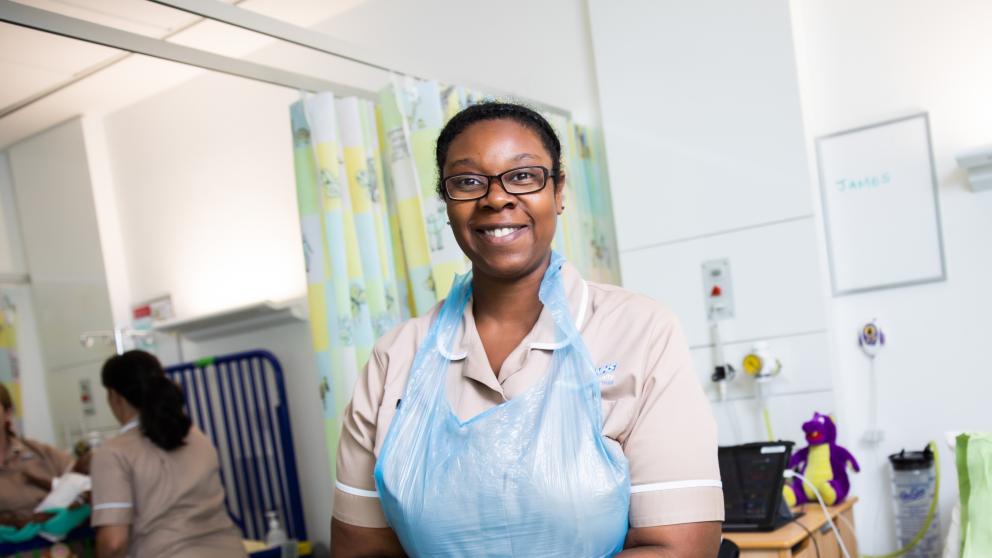 Female Nursing Associate apprentice putting on gloves in a simulated ward environment