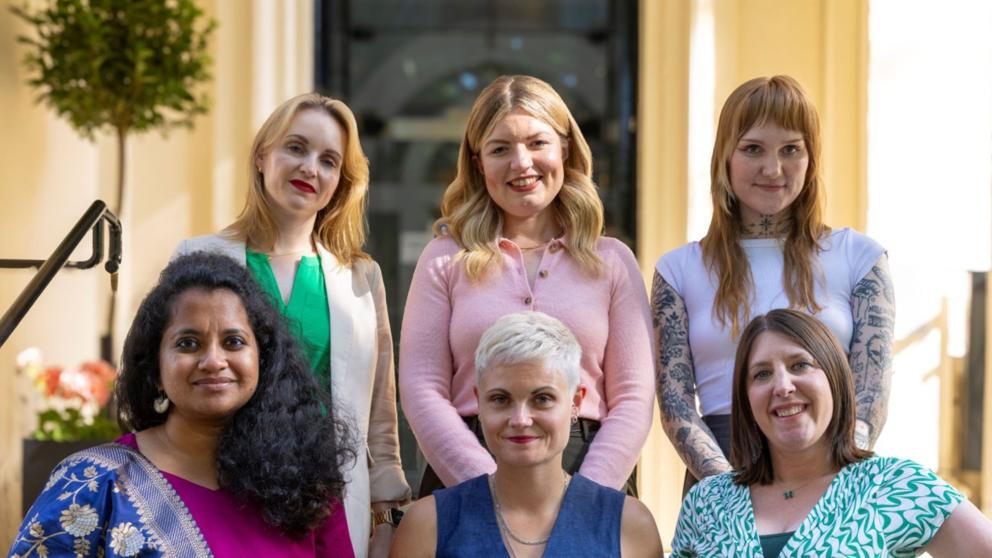 A line of six women pose in sets of three for a photo