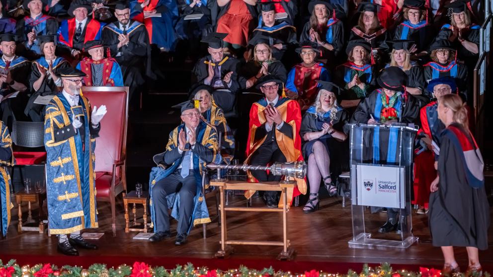 Graduate walks across stage towards the Vice-Chancellor during Graduation Ceremony as the processions applauds from the back of the stage 