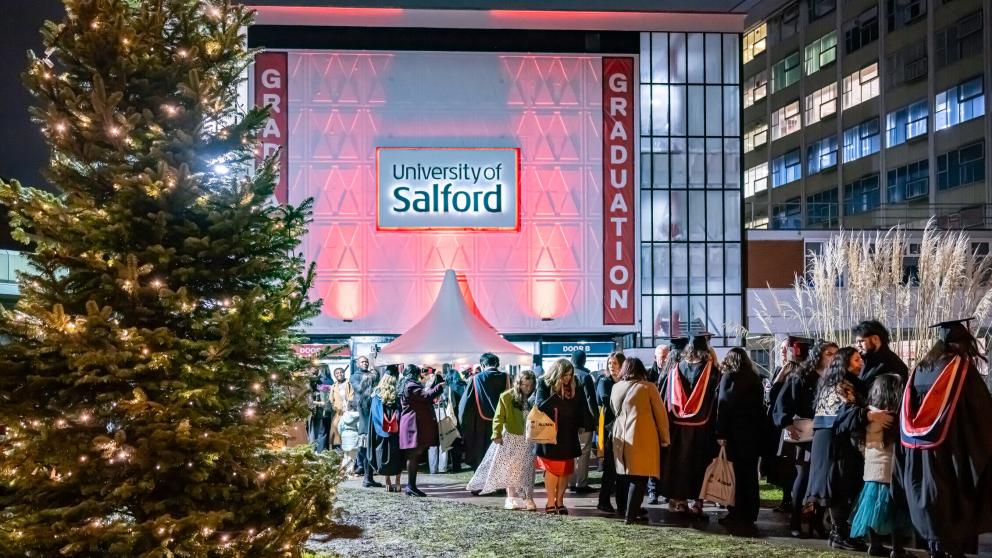 Guests and graduates entering Maxwell Hall with a christmas tree outside