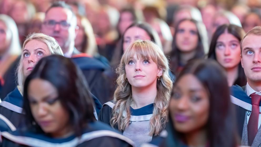 Graduate looks up at stage from the graduation crowd