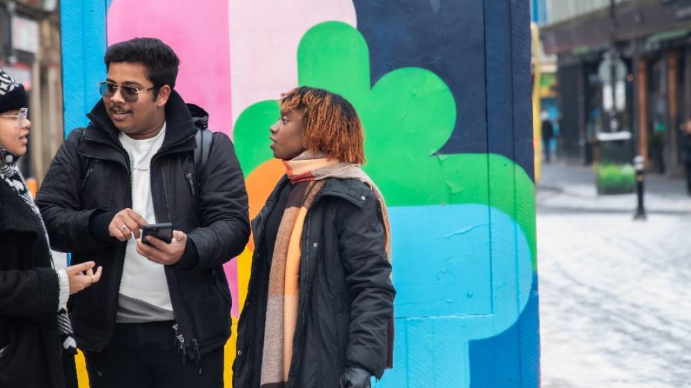 Three international students looking at a phone in Stevenson Square
