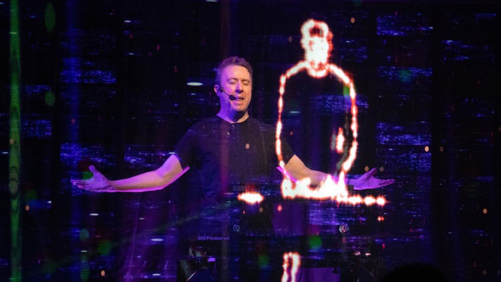 A man performs next to a holographic figure