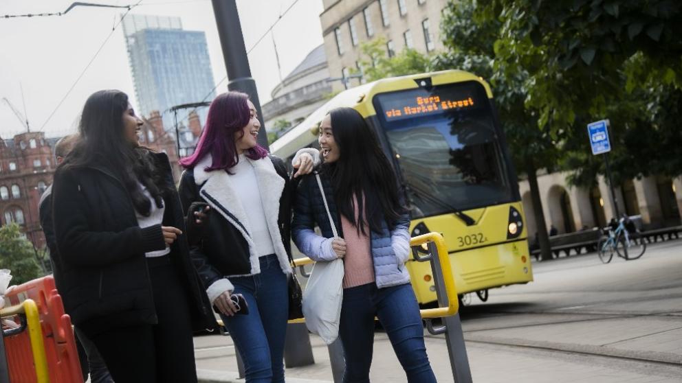 Three students walking around Manchester city centre alongside a tram