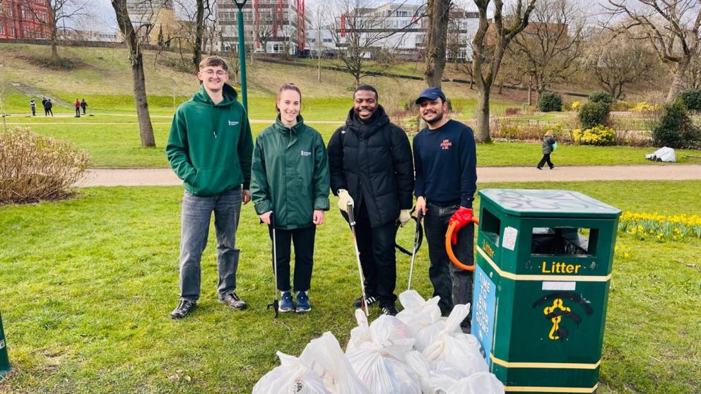 People standing next to a rubbish bin in Peel Park, holding litter pickers and smiling.
