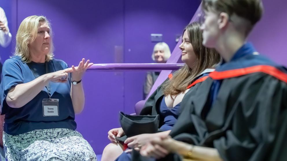 A British Sign Language Interpreter faces two graduates in the theatre. 