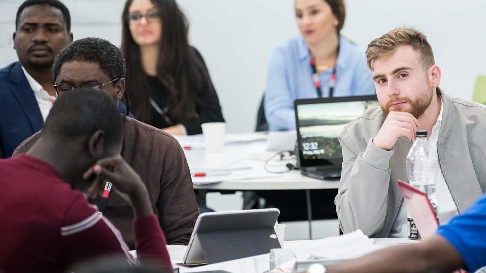 Six students in a lecture with laptops, tablets and note books