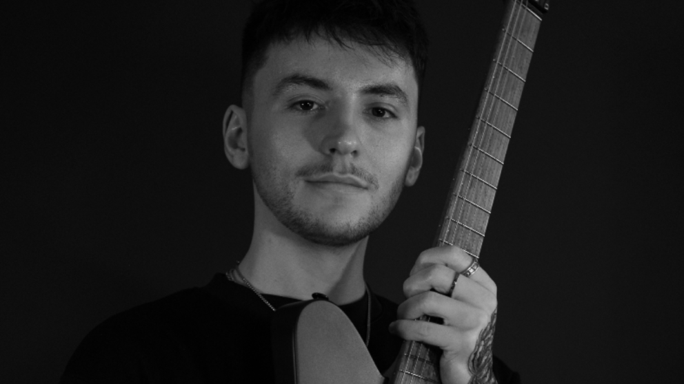 A man hold a guitar and faces the camera