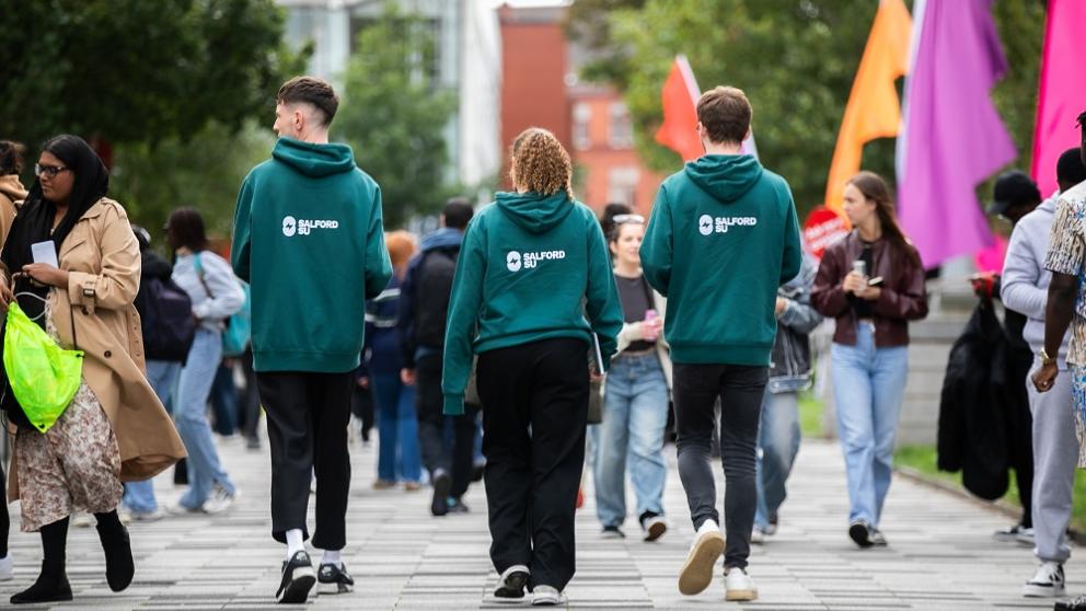 Three staff members wearing Salford SU hoodies walking through campus during Welcome Week