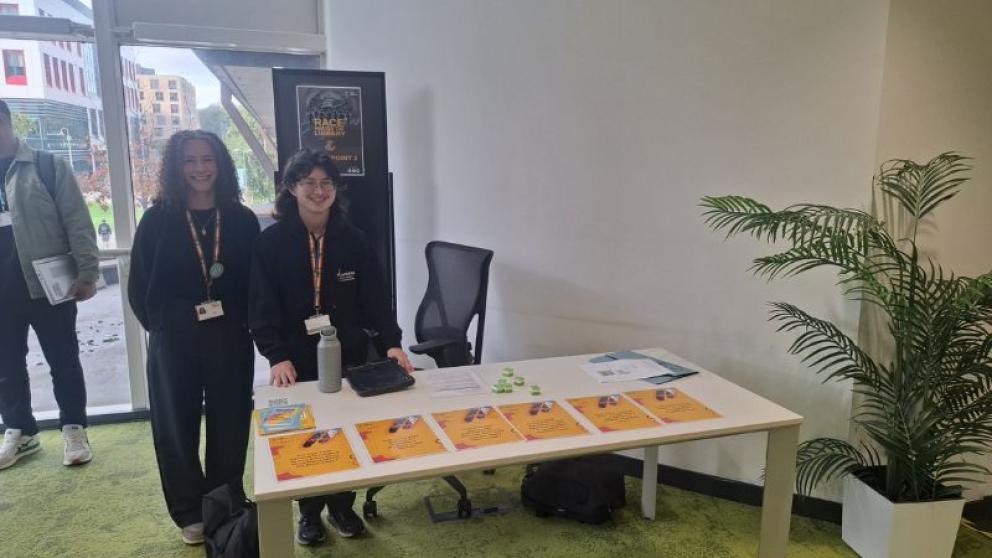 Two members of staff at a informational desk with cards on it