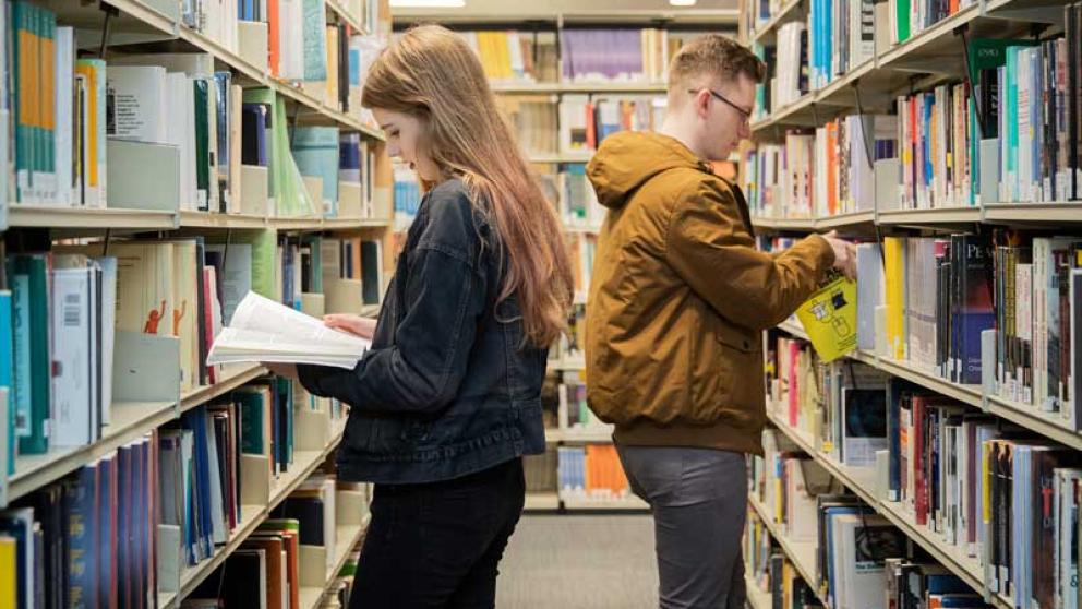 Two students selecting books from shelves in Clifford Whitworth Library