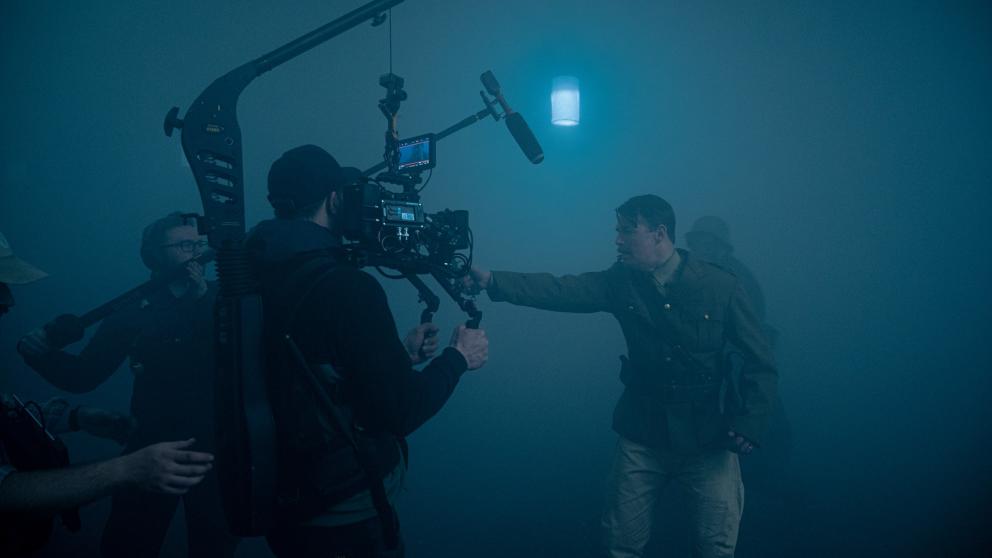 An actor holds a gun in a foggy sounds stage