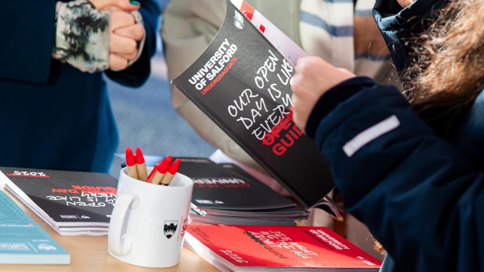 A member of staff flicking through the Open Day guide at the Open Day check-in desk