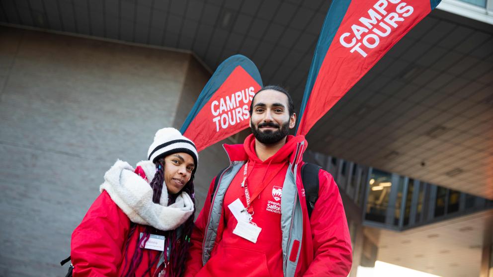 Two student ambassadors wearing branded red hoodies and jackets at the University of Salford