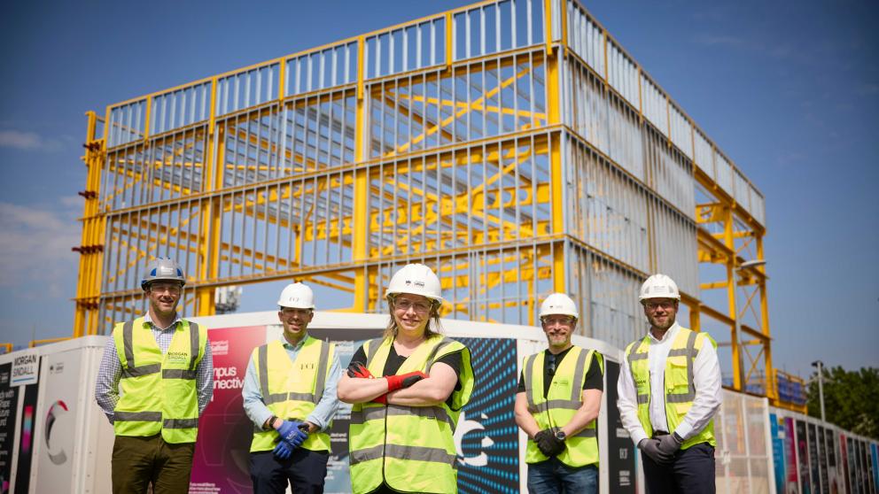 Figures stand in front of the Acoustics building steel frame