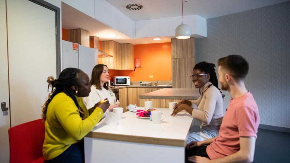 Group of four students sitting round a kitchen table eating and drinking