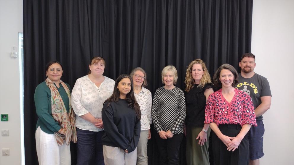 This image shows a group of people standing in front of a dark curtain